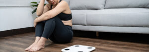 woman sitting on the ground looking nervous next to a scale