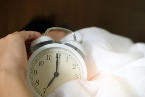 man holding old fashioned alarm clock in bed