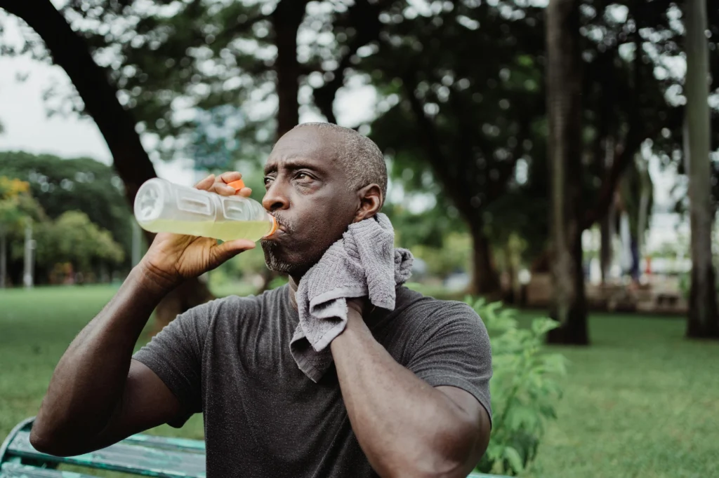 man drinking liquids and wiping away sweat during exercise