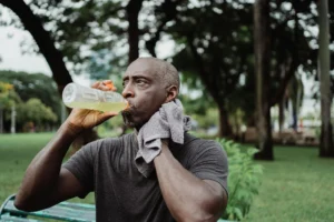 man drinking liquids and wiping away sweat during exercise