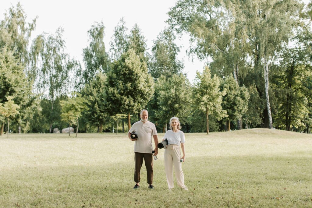 older couple standing in field holding yoga mats